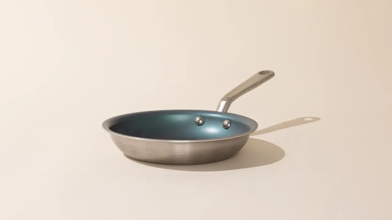 A stainless steel frying pan with a blue interior and a silver handle on a neutral background.