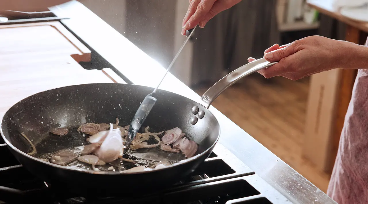 A person's hands are sautéing food in a pan on a stove.