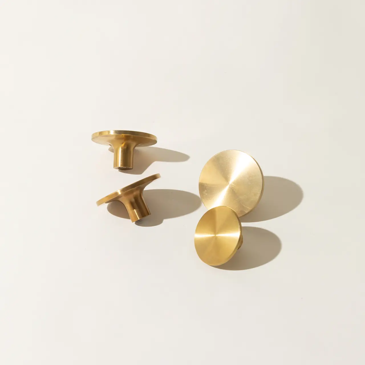 Three modern, circular brass knobs of varying sizes displayed on a light surface, casting soft shadows.