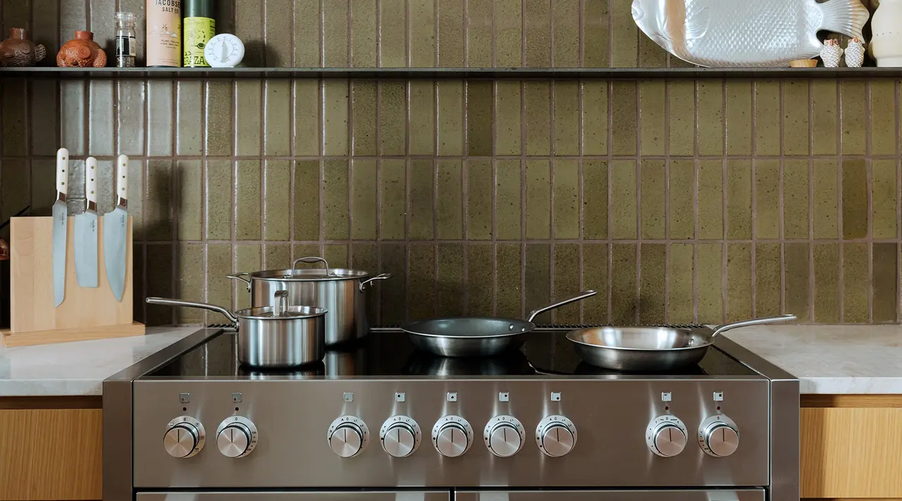 A stainless steel stove with pots and pans sits against a tiled backsplash, reflecting a modern kitchen setting.