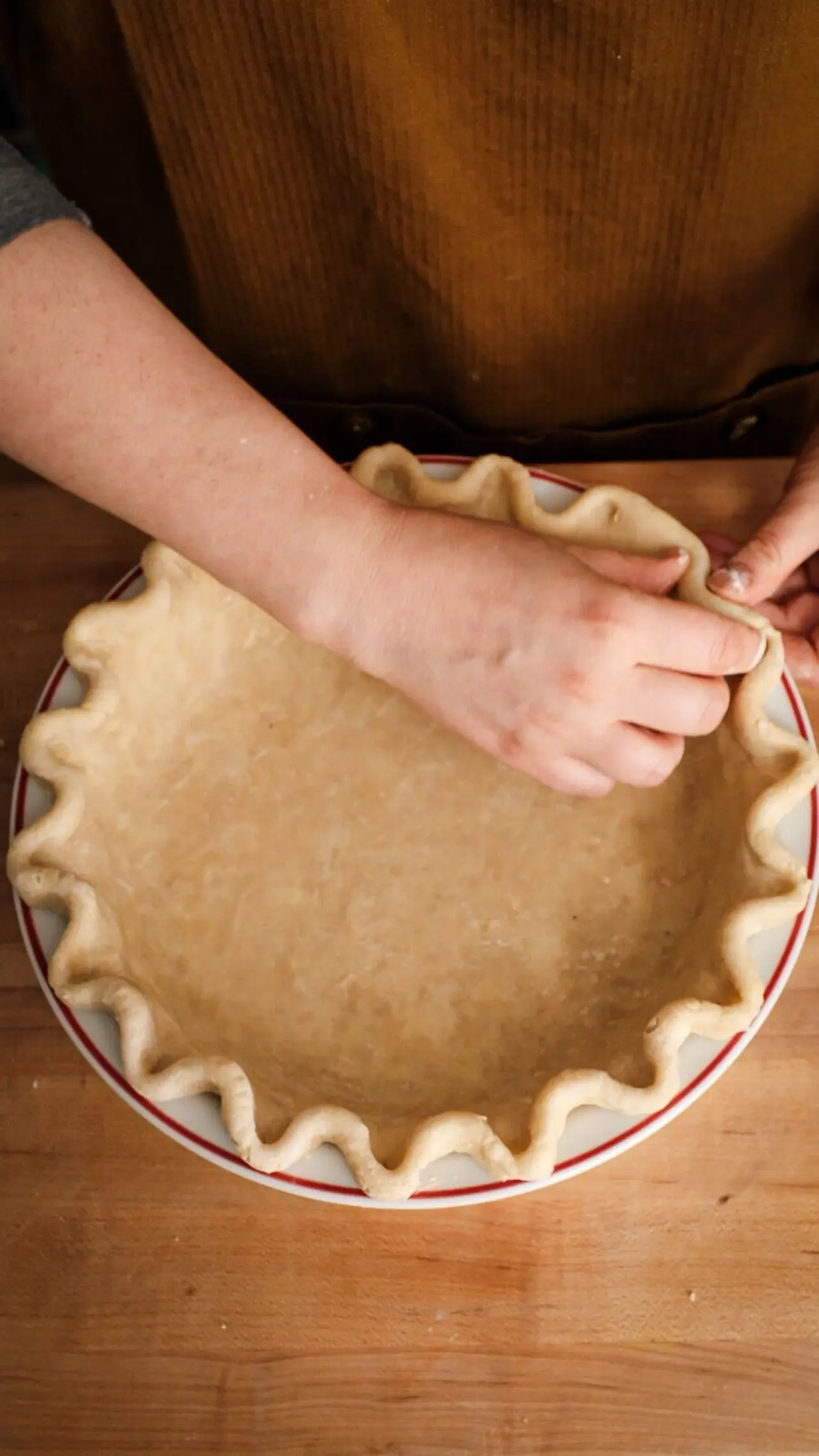 A person shapes the edges of a raw pie crust in a round pie dish.