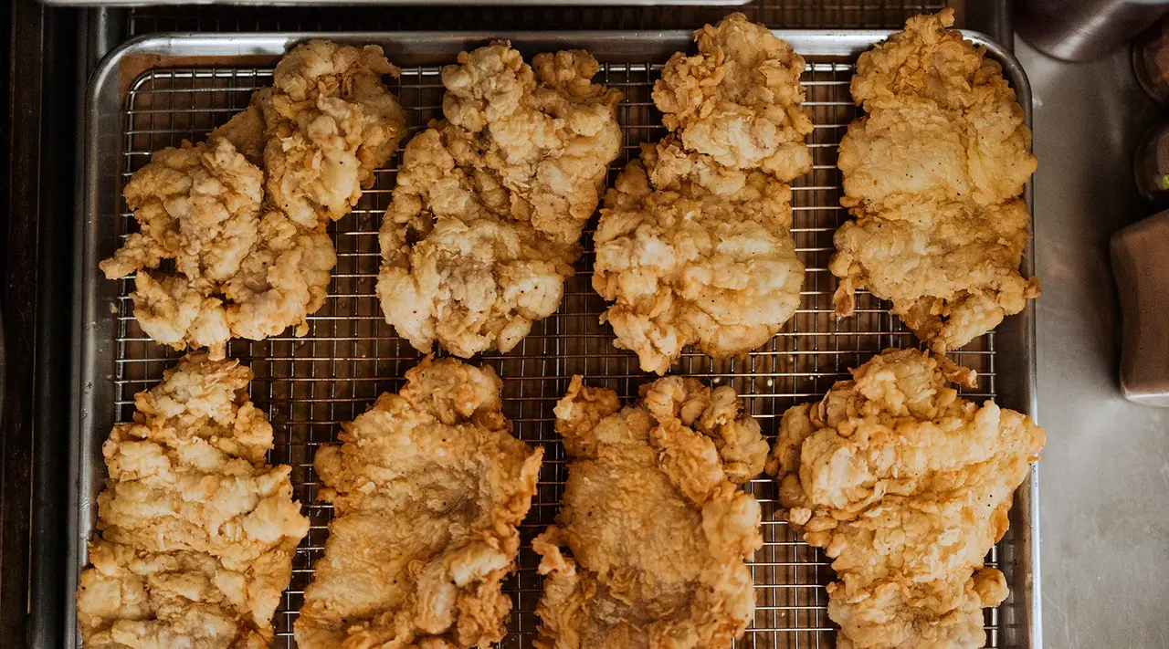 Golden-brown fried chicken pieces are cooling on a wire rack over a baking sheet.