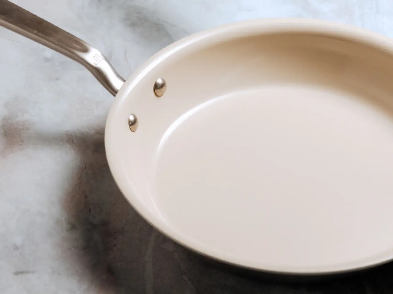 A ceramic non-stick frying pan with a metal handle lies on a marble surface.