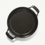 A round cast iron pan with two side handles, featuring a smooth black interior.