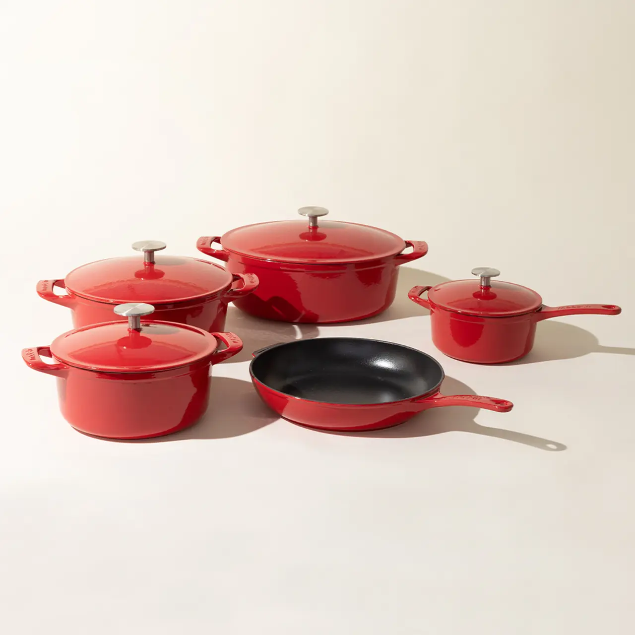A set of red cookware with various pots and a pan, each with matching lids, displayed against a neutral background.