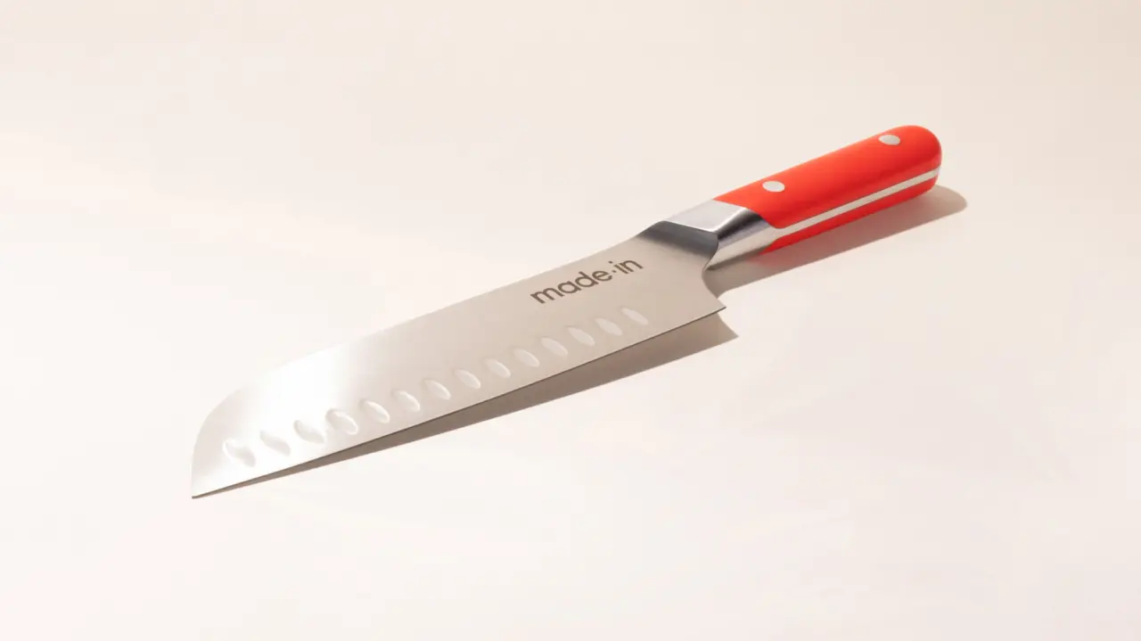 A stainless steel chef's knife with a red and silver handle lies on a white surface.