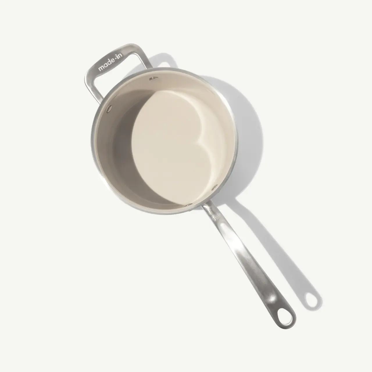 A stainless steel saucepan with a long handle is shown from a top-down perspective, featuring a smooth, reflective interior.