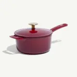 A vibrant red saucepan with a gold knob on the lid and a long handle, sitting on a light background.