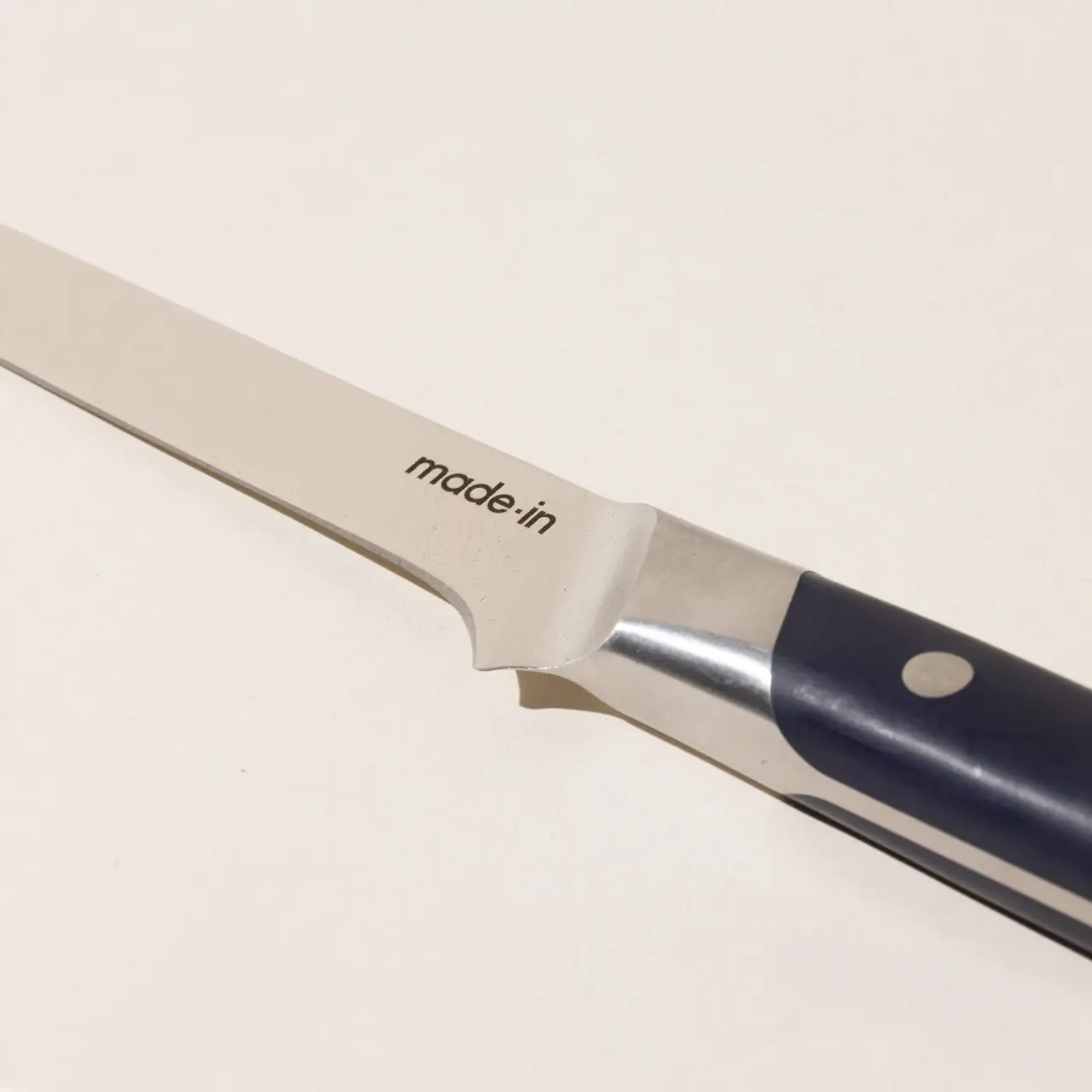 A close-up of a kitchen knife with the text "made-in" on the blade against a plain background.