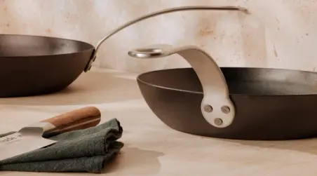 Two non-stick frying pans on a counter with a dark green cloth and a wooden-handled knife nearby.