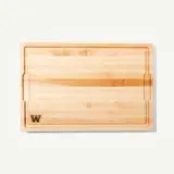 A wooden cutting board featuring a smooth surface and a decorative inlay, marked with a letter "W."