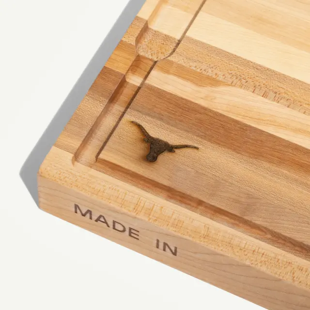 Close-up of a wooden cutting board featuring a small logo of a longhorn and the inscription "MADE IN."