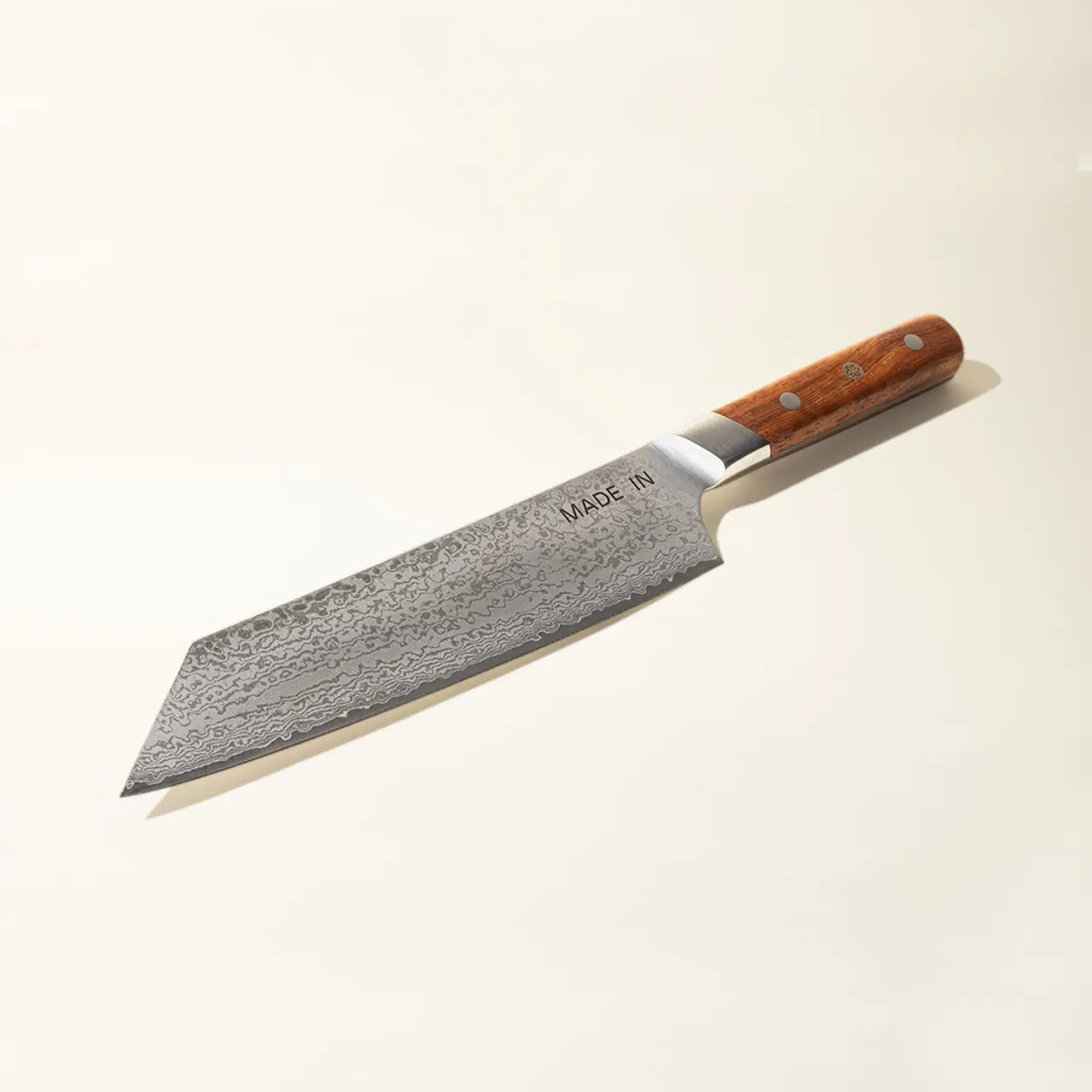 A finely crafted chef's knife with a damascus pattern blade and a wooden handle rests against a light background.