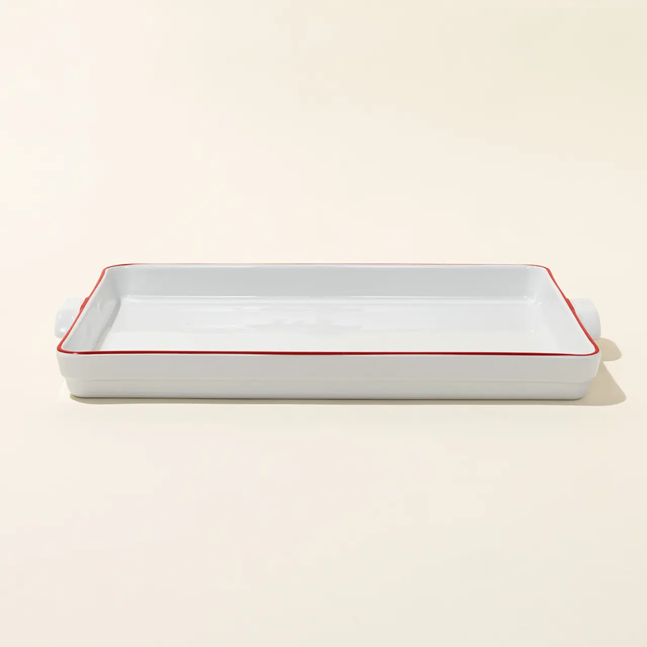 A rectangular, white ceramic baking dish with red trim sits on a neutral background.