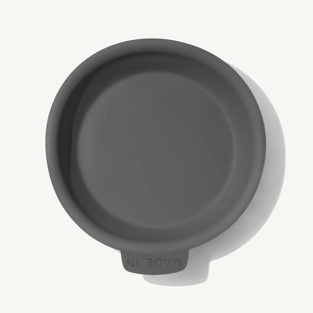 A top view of a round, dark-colored, silicone or rubber lid marked with the text "MADE IN."