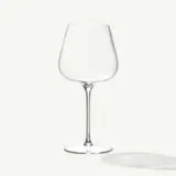 A clear, empty wine glass with a long stem casts a soft shadow on a plain white background.