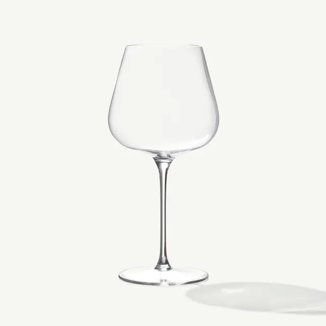 A clear, empty wine glass with a long stem casts a soft shadow on a plain white background.