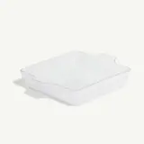 A white, square ceramic baking dish with handles on two sides and a textured exterior is placed on a plain background.