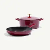 A shiny red cooking pot with a lid and a matching skillet are displayed together.