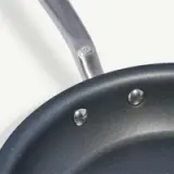 Close-up of a non-stick frying pan with a metal handle attached by rivets.