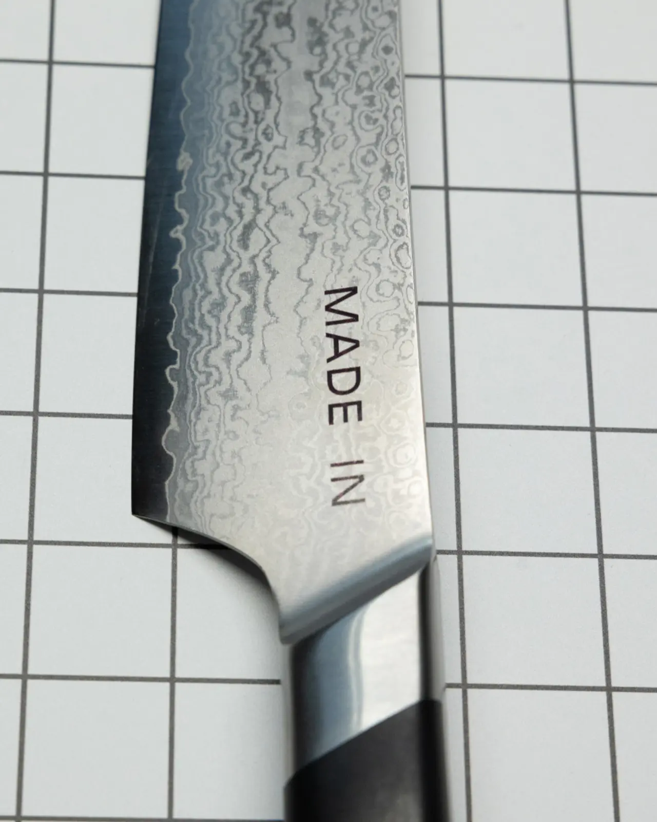 A close-up photo of a patterned kitchen knife blade engraved with the words "MADE IN."