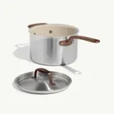 A stainless steel cooking pot with a cream-colored interior and a matching lid sits on a light background.