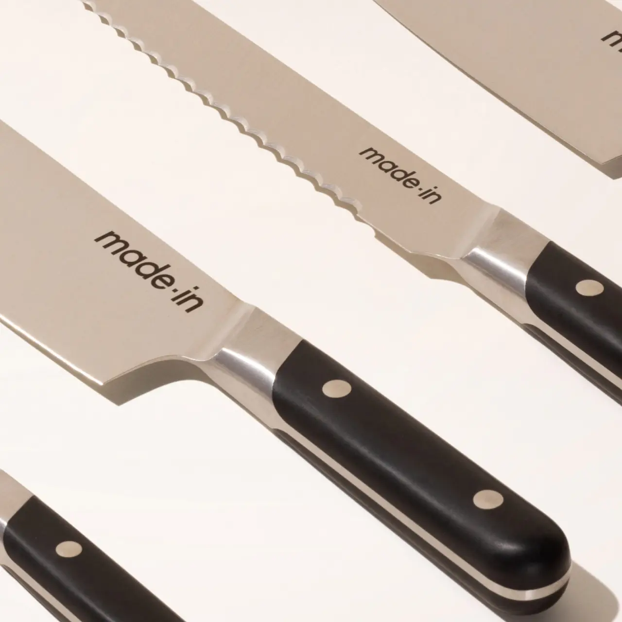 Two serrated kitchen knives with black handles and the inscription "made in" on the blade, angled and overlapping each other on a plain background.