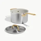 A stainless steel cooking pot with a gold-colored handle and a matching lid rests beside it.