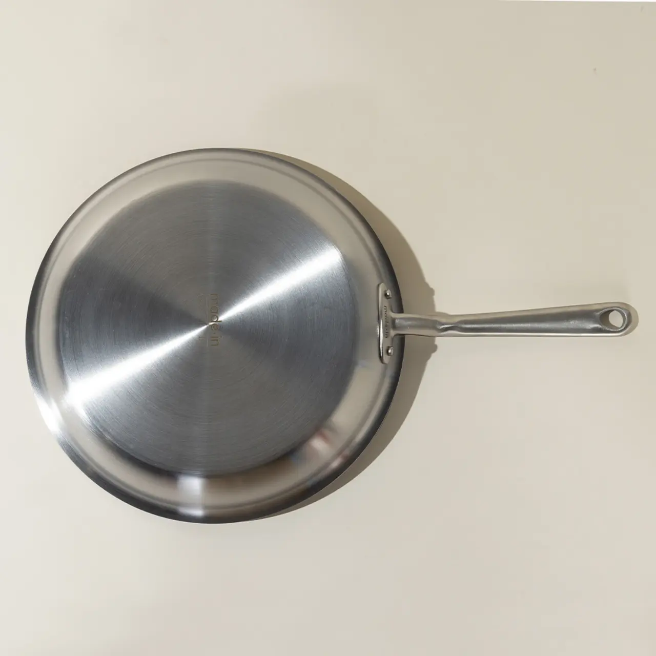 A stainless steel frying pan with a long handle is shown from above on a plain background.