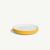 A stack of four white plates with yellow rims is displayed against a plain background.