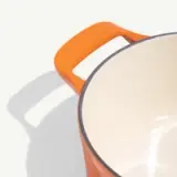 A vibrant orange cooking pot with a smooth interior and dual handles sits against a light background.