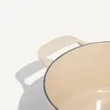 A light-colored cooking pot with a curved design and a handle rests on a muted background.