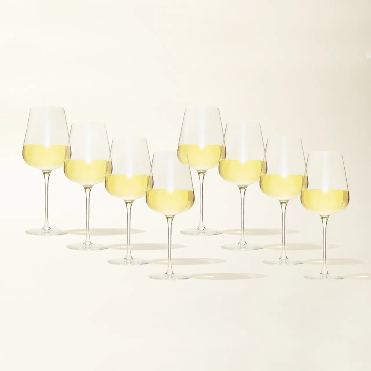 Several wine glasses filled with white wine are arranged in a row on a light background.
