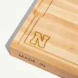 A wooden cutting board features an engraved letter "N" and the text "MADE IN" on the side.