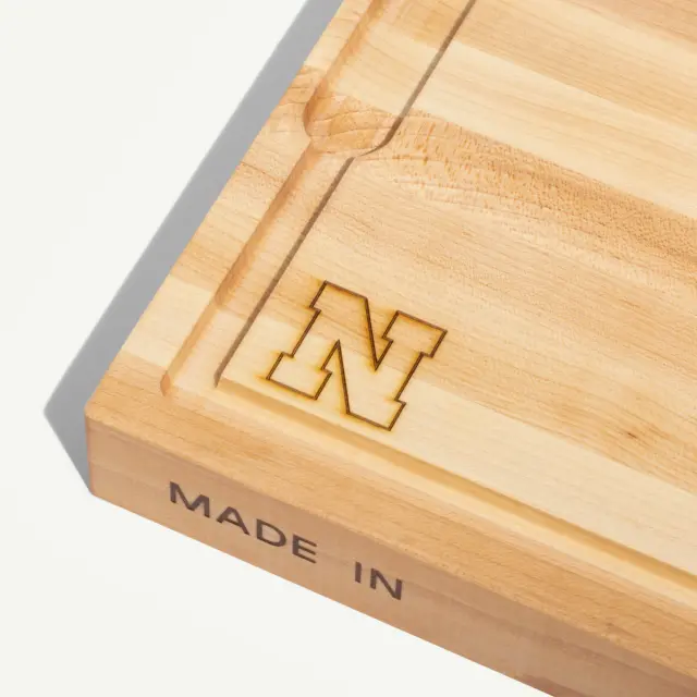 A wooden cutting board features an engraved letter "N" and the text "MADE IN" on the side.