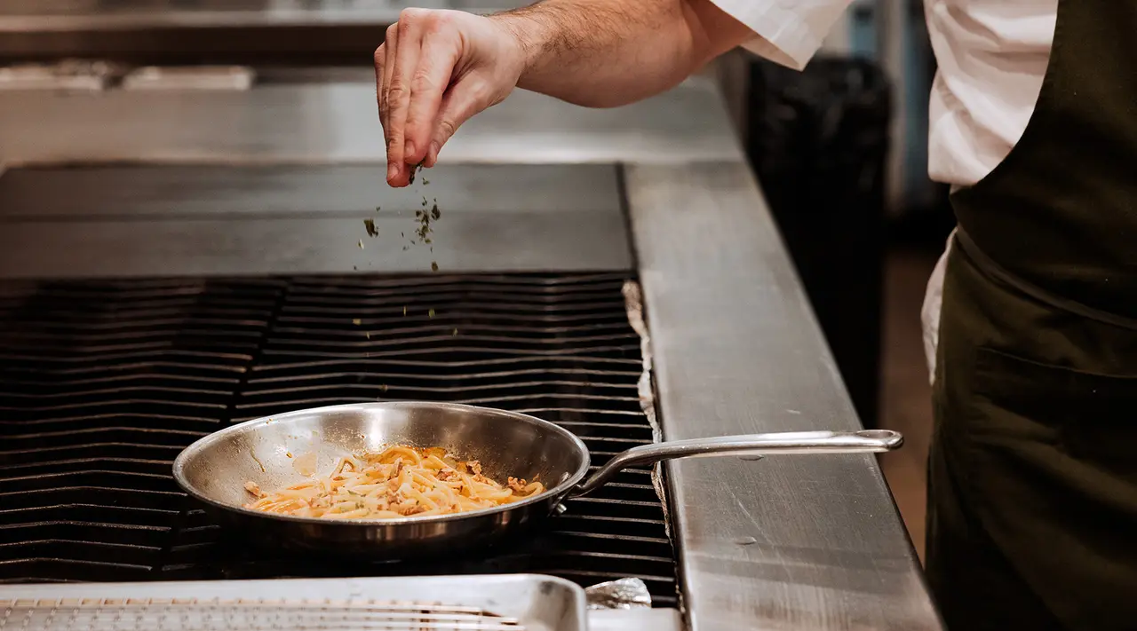 A chef is seasoning food in a pan on a stove.