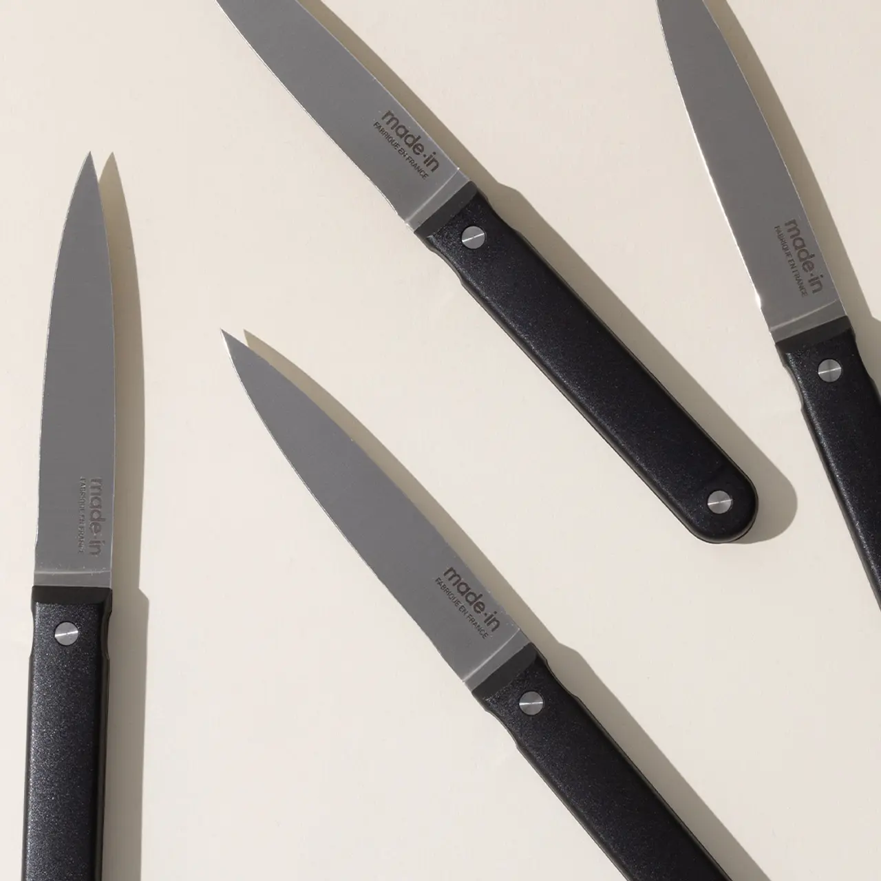 Three black-handled kitchen knives with stainless steel blades are laid out diagonally on a light background.