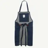 A denim apron with a grey interior, featuring a waist tie and a small label at the top.