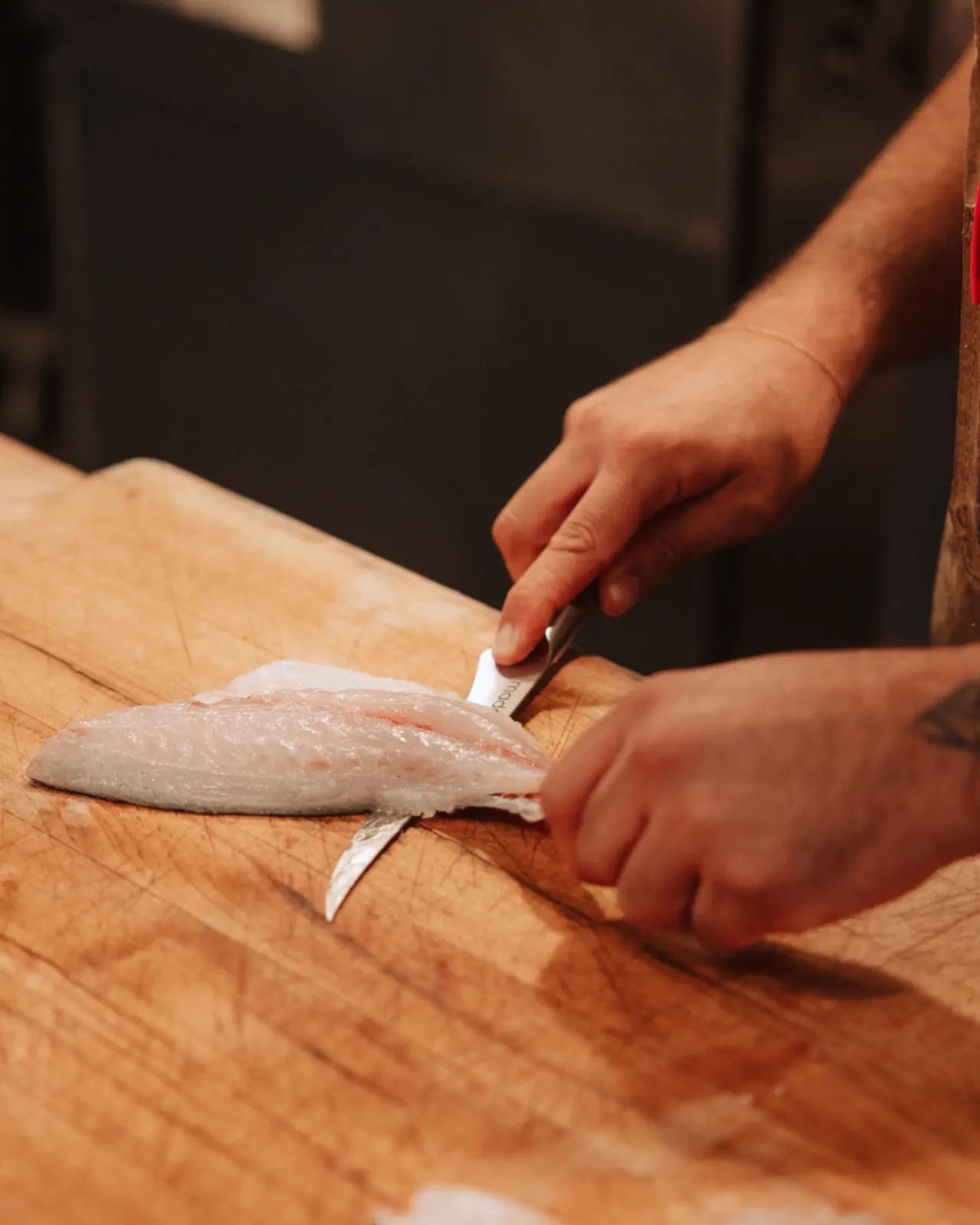 A person is skillfully filleting a fish on a wooden cutting board with a sharp knife.