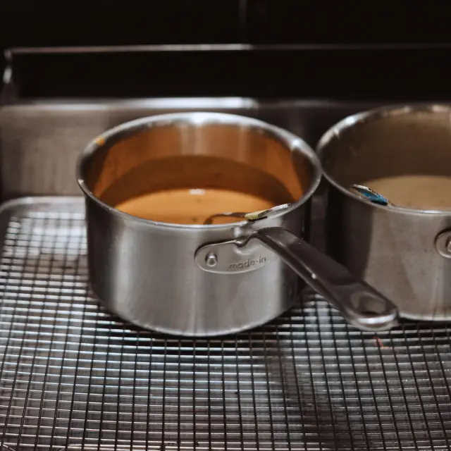 Two stainless steel pots filled with different colored mixtures are resting on a wire cooling rack.