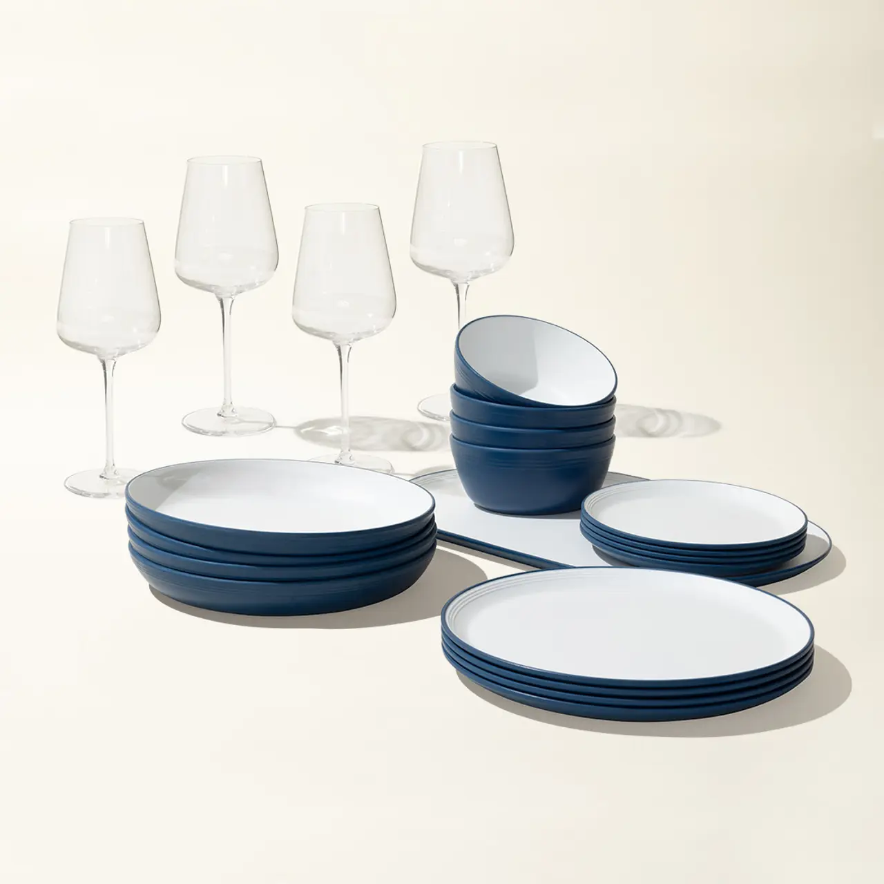 A set of elegant blue and white dishes is neatly arranged with a quintet of clear wine glasses on a light background.