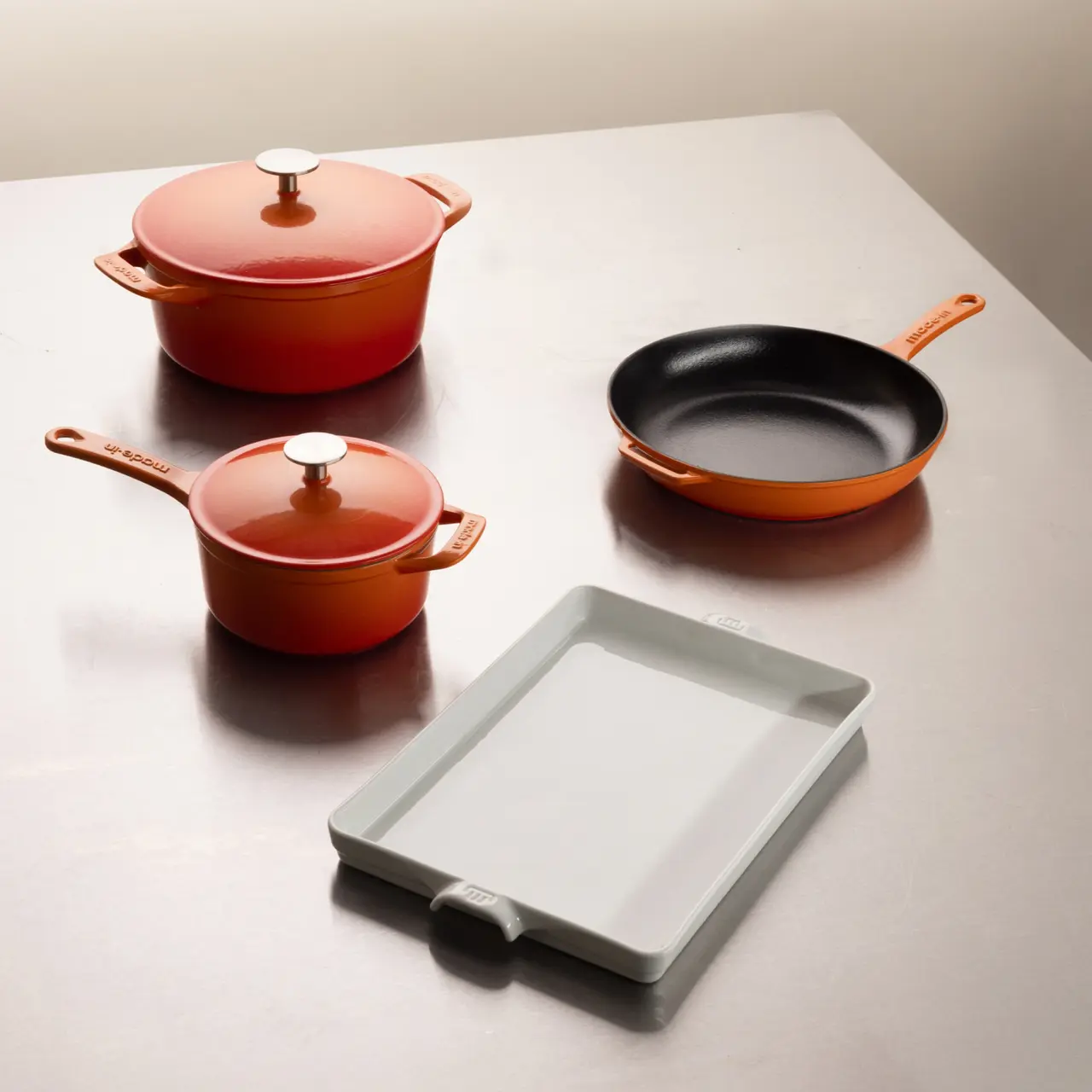 Three colorful cooking pots and a rectangular baking dish are arranged on a smooth surface.