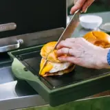 A person is cutting a sandwich with melted cheese and an egg on a griddle.