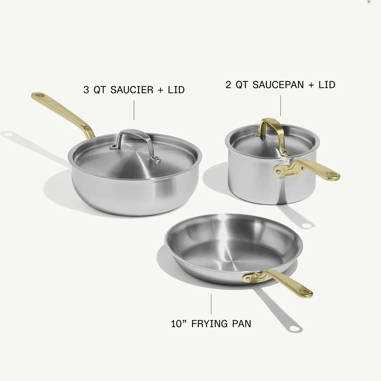 A collection of three stainless steel cookware items includes a 3-quart saucier with a lid, a 2-quart saucepan with a lid, and a 10-inch frying pan, all featuring golden handles.