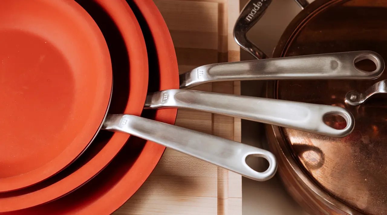 A stack of red frying pans with silver handles is neatly organized in a kitchen drawer alongside other cookware.