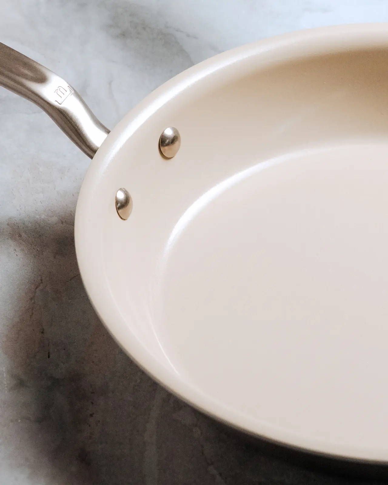 A close-up view of a white ceramic frying pan with a stainless steel handle.