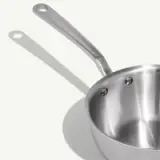 A stainless steel saucepan with a long handle and a shadow cast to the left.