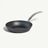 A black frying pan with a long, curved handle is shown against a plain background.
