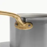 A stainless steel pot with a gold-tone handle features the text "mode-in" embossed on the side.
