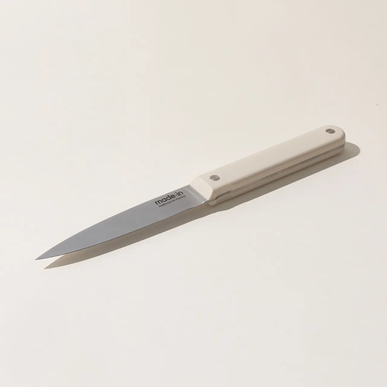 A simple paring knife with a silver blade and a beige handle lies on a plain white background.